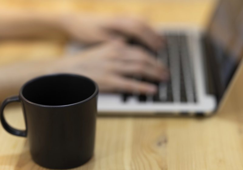 Person typing on a laptop with a coffee cup nearby