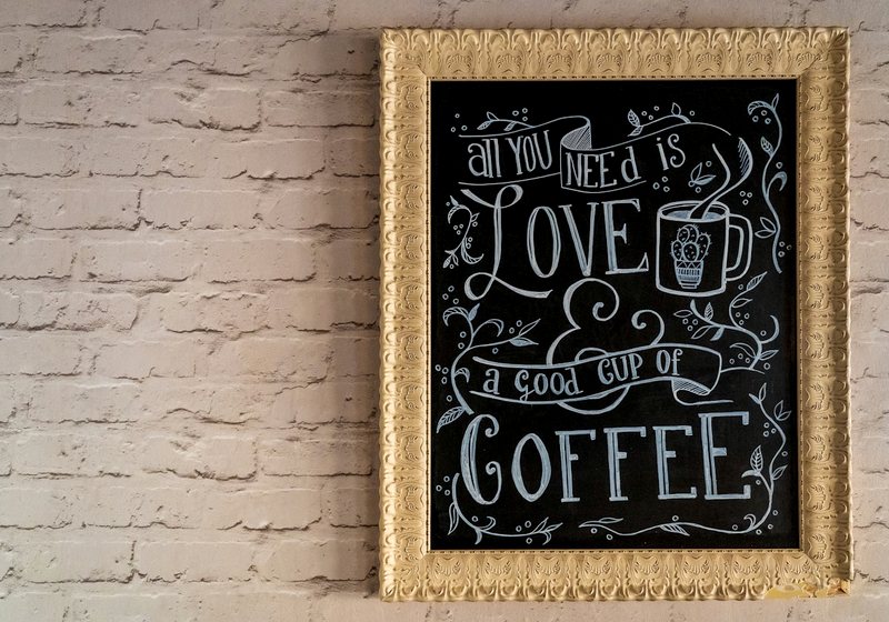 Decorative chalkboard-style coffee sign on a brick wall