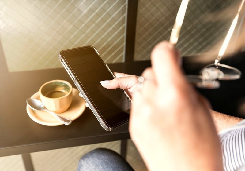 Person checking a phone next to a coffee cup at a restaurant table