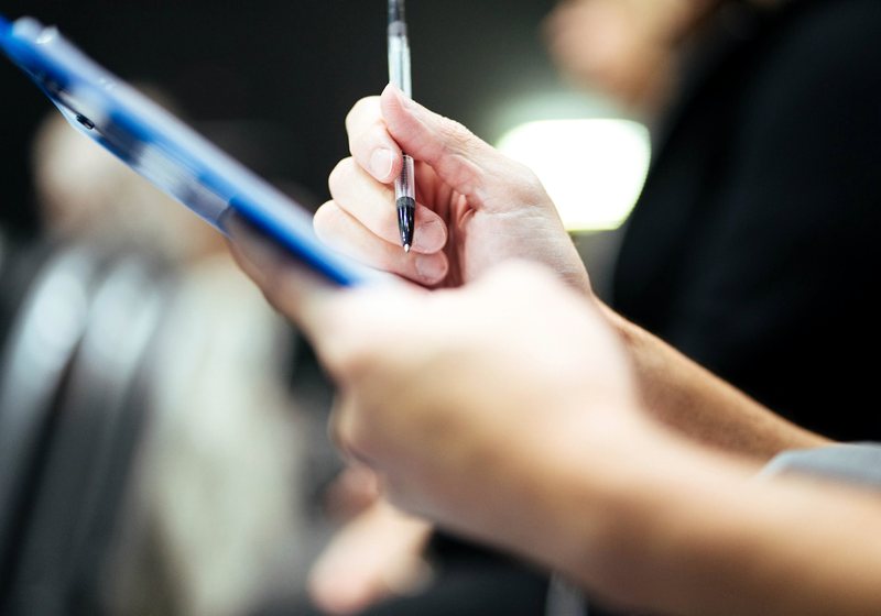 Hand holding a pen over a clipboard, taking notes